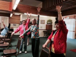 Low vision support group members doing chair yoga led by Mina Izadsepas.