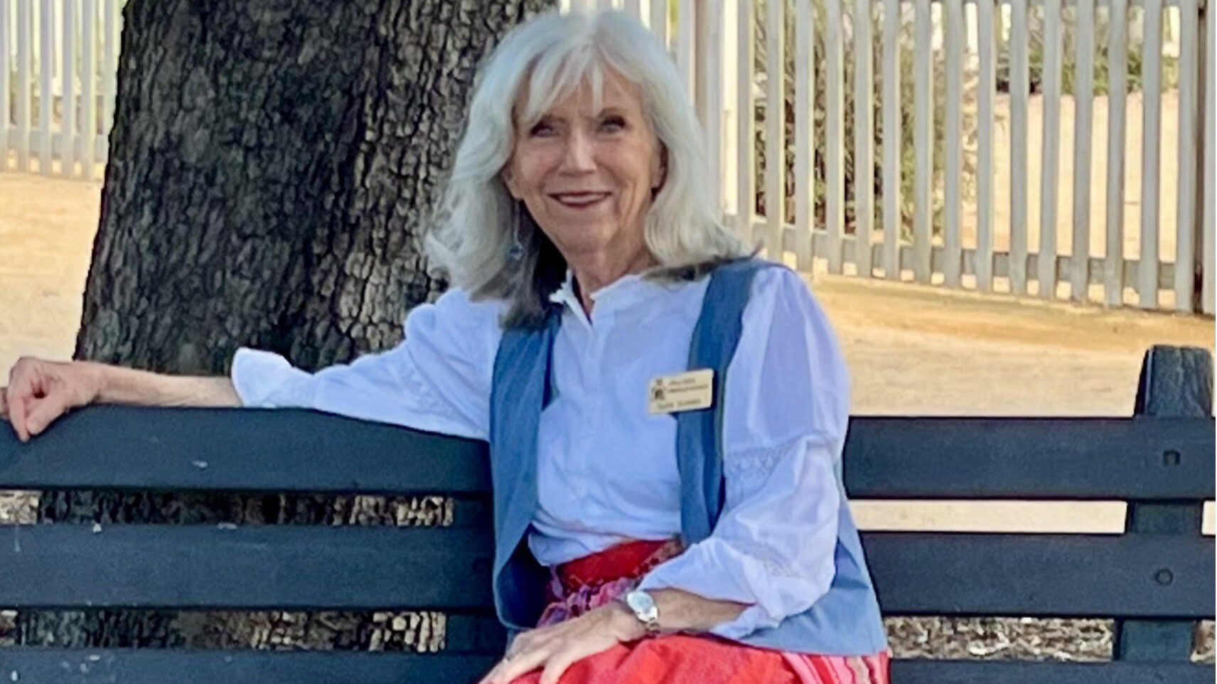 Susan Muhrer, smiling, sitting on a bench outdoors.