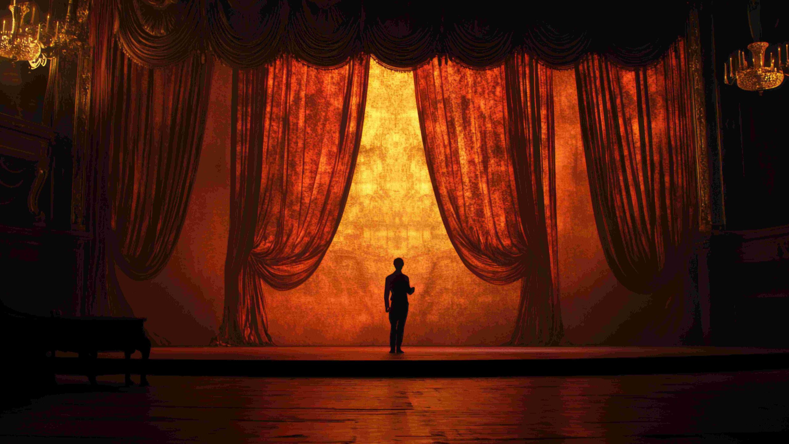 Theater stage with draped and opened curtains and lone figure standing on stage.
