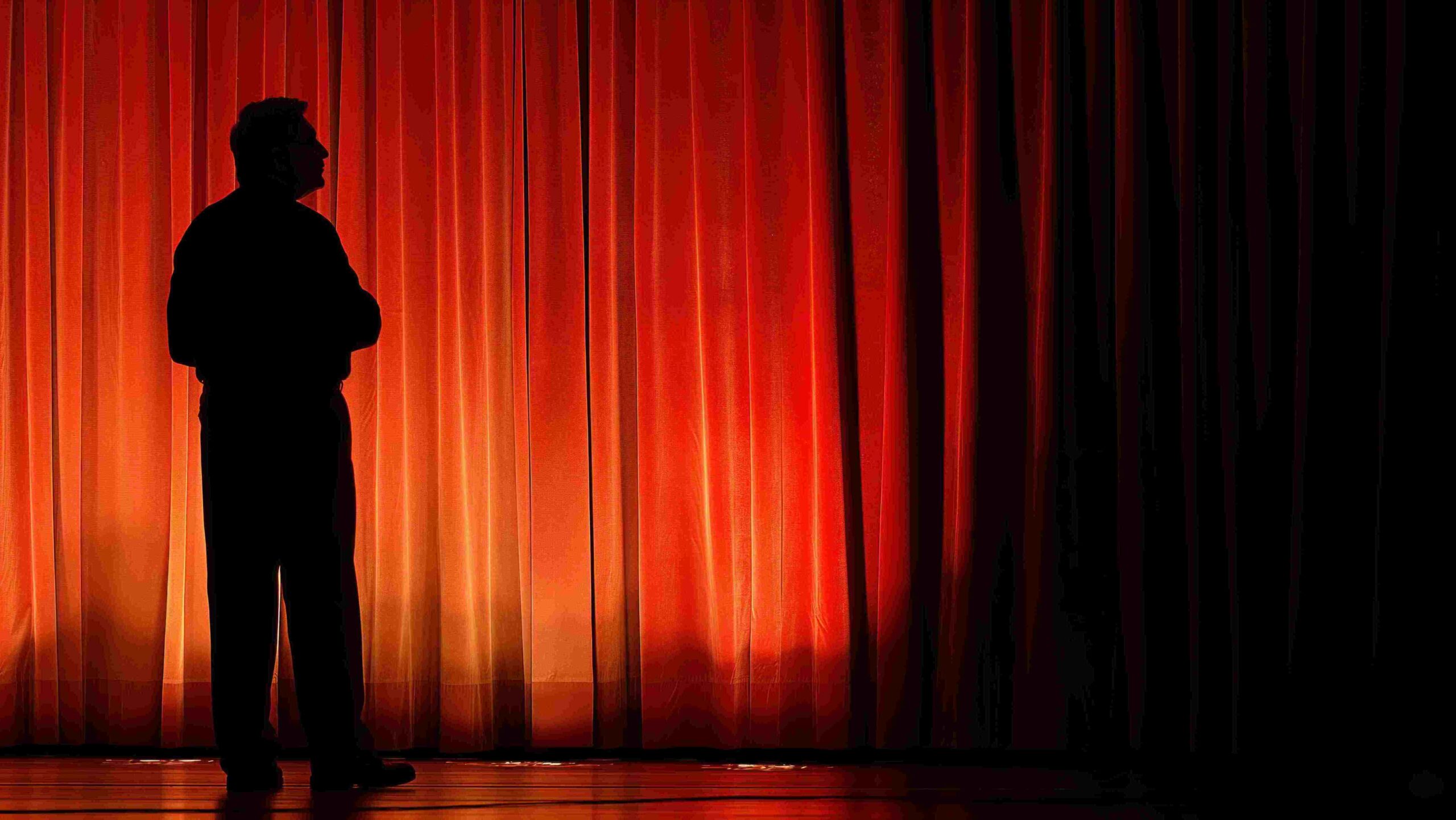 Red theater curtains and silhouette of man on stage.