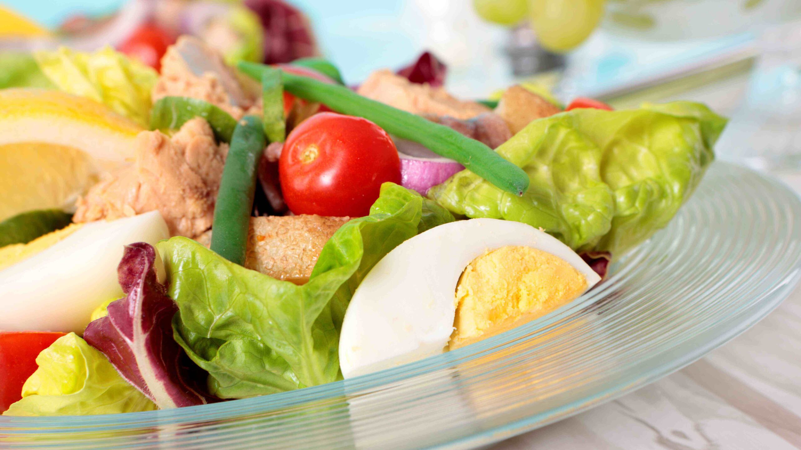 Close up of a salad in a glass bowl with lettuce, tomatoes and boiled eggs.