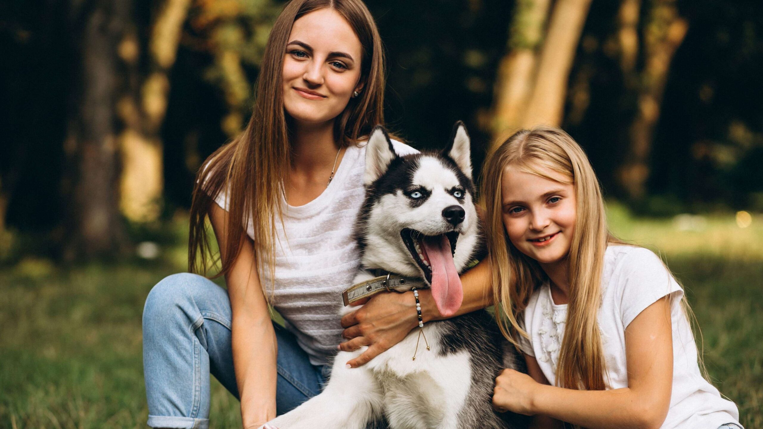 Two young women outdoors hugging a Huskey dog.