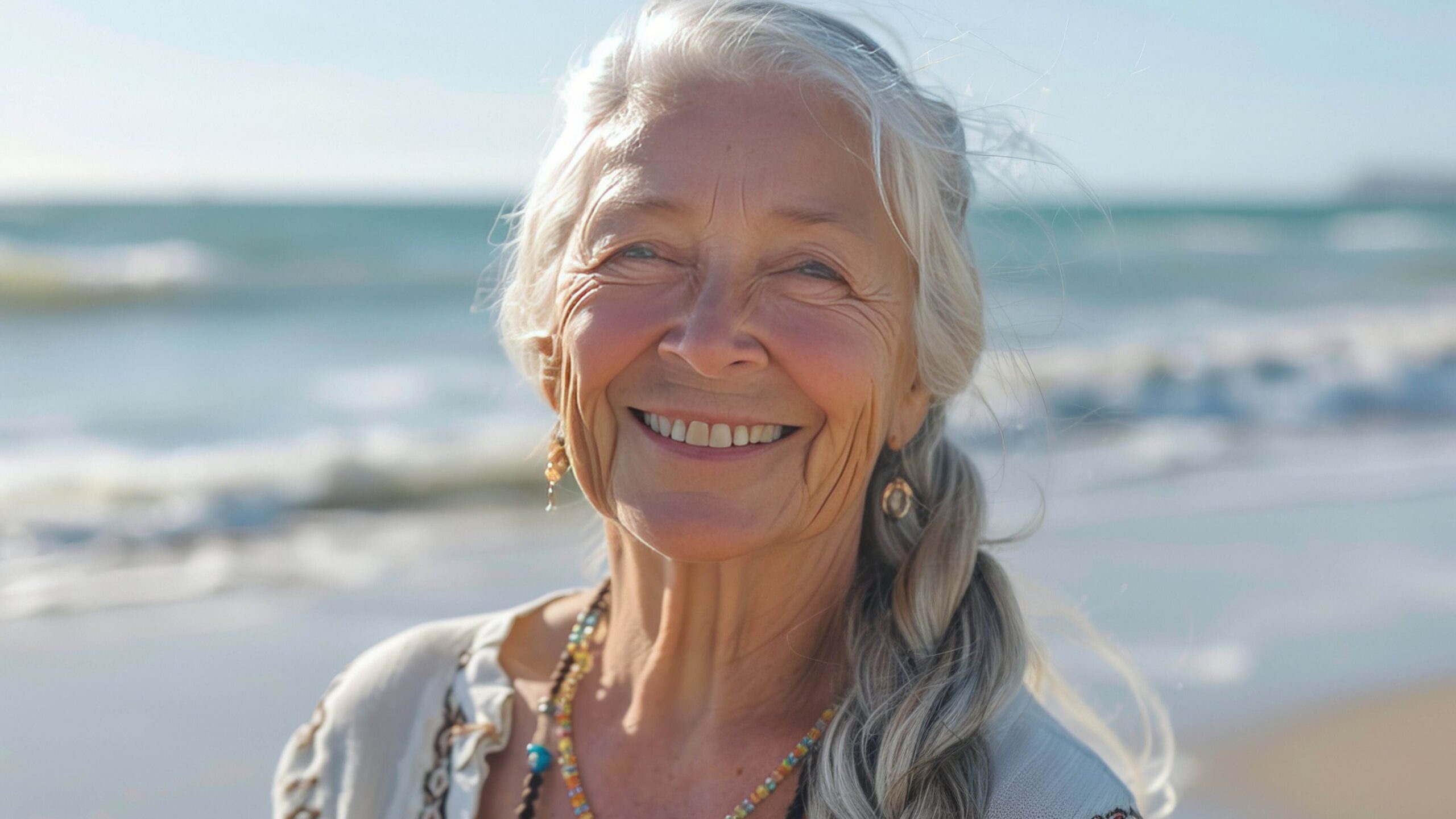 Serene, smiling woman on a beach with braided silver hair.