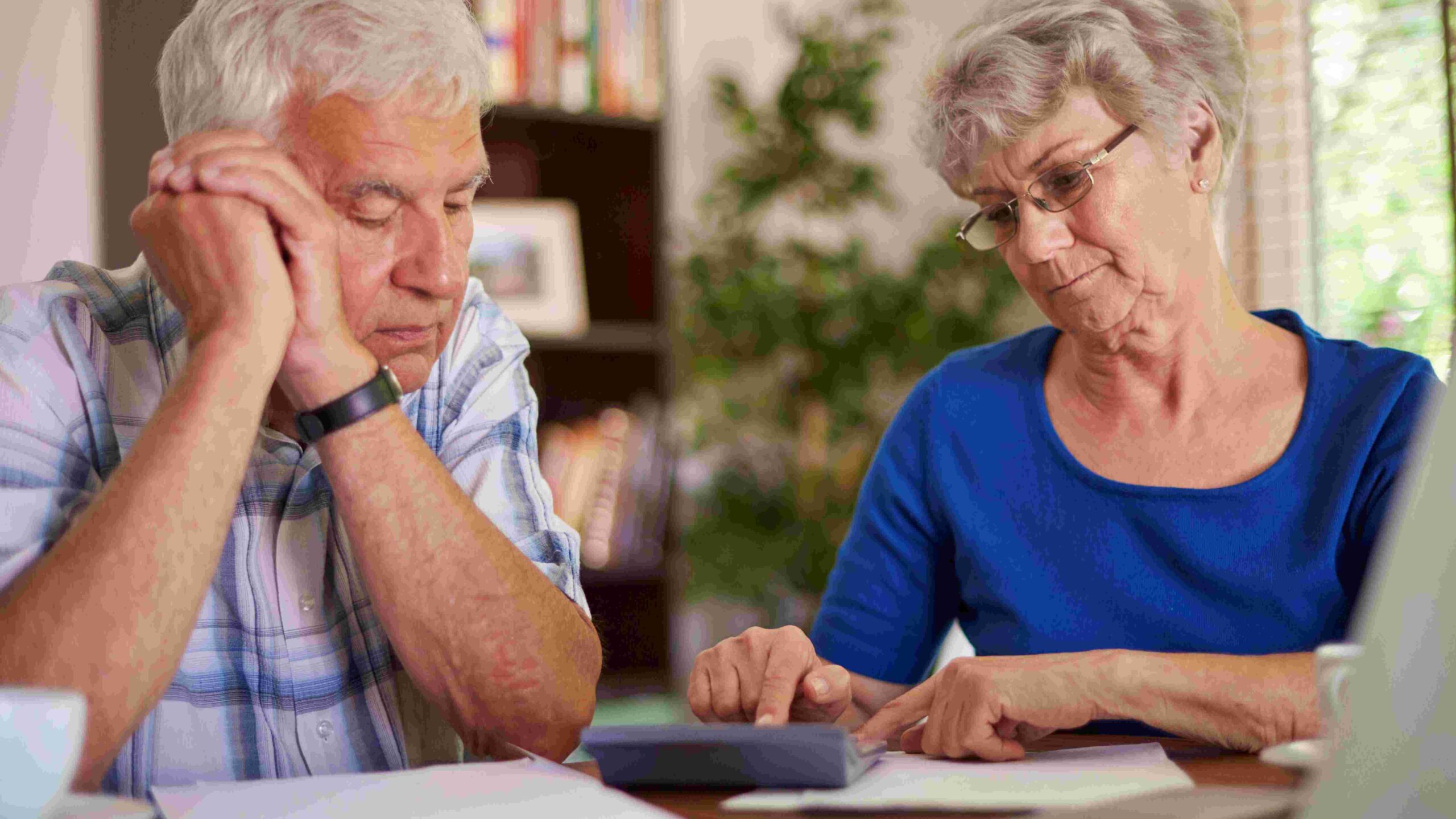 Senior man and woman looking at paperwork and using a calculator.