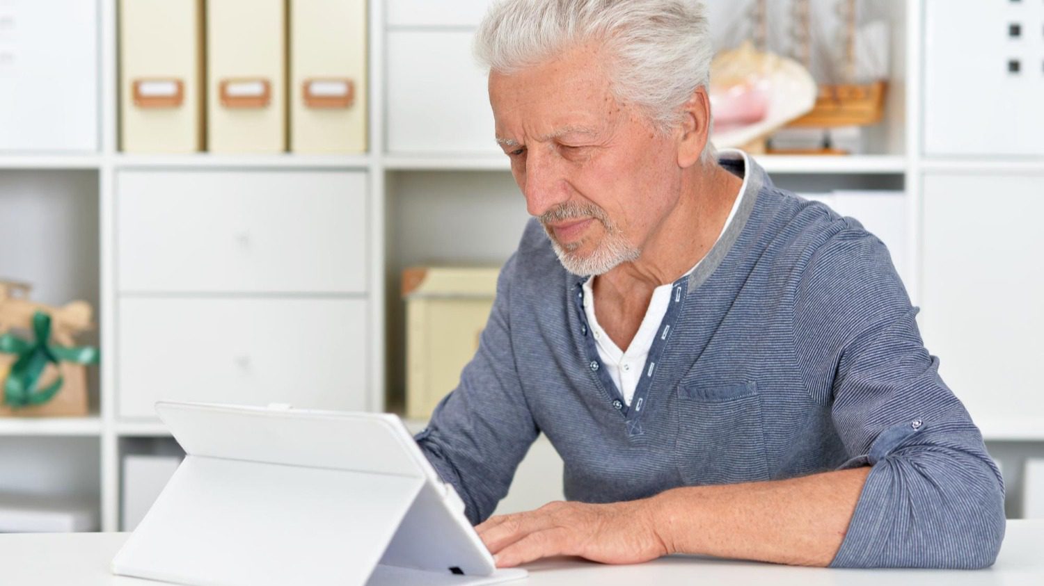 Senior man sitting in a room and looking at a laptop.