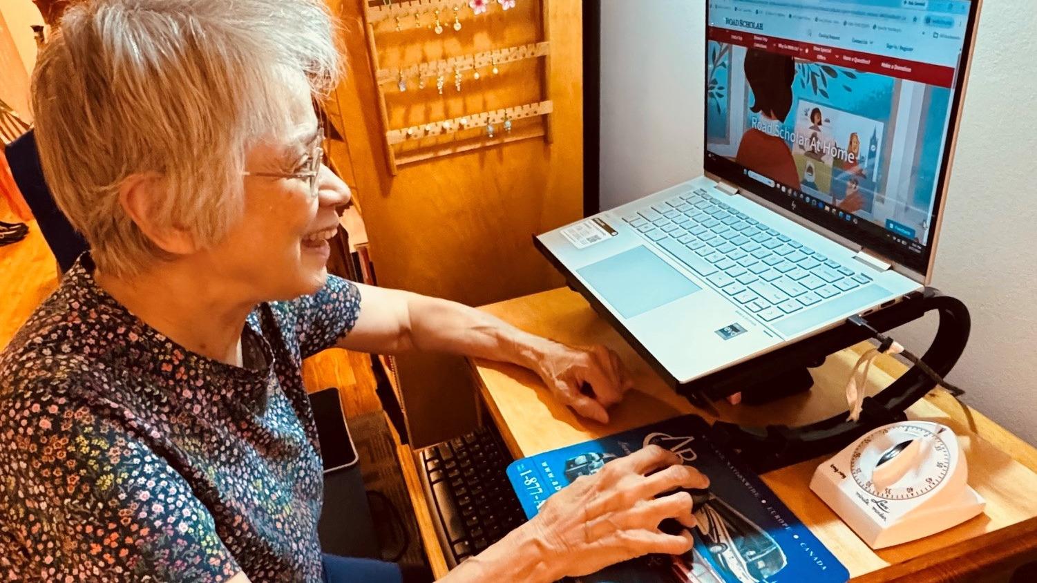 Senior woman smiling as she watches online lecture on her computer screen.